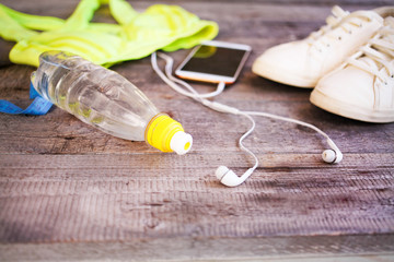 Water bottle, women's clothing for sport, white sneakers and earphones on a wooden background