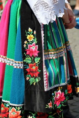 Kobieta (dolna część ciała) ubrana w tradycyjny strój ludowy z regionu Łowicza, polska, pasiasta kolorowa spódnica haftowana w kwieciste wzory - obrazy, fototapety, plakaty