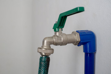 faucet and green hose attached to the blue poly pipe on white wall. close up selective focusing.