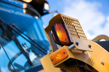 Yellow warning lights on excavator. Road construction workers repairing highway road on sunny summer day. Loaders and trucks on newly made asphalt. Heavy machinery working on street.  