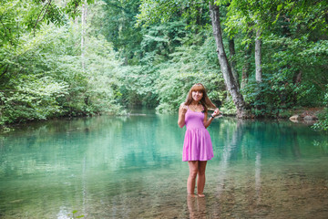 girl in a pink short dress walks on a river in the forest