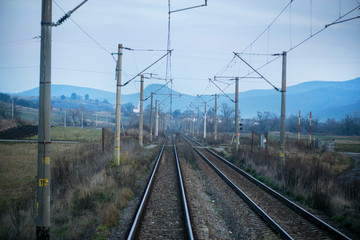 Fototapeta premium Eastern European railroad across Transilvania. Mountain landscape in the background. Scary, dangerous scene in winter with naked trees and polluted nature 