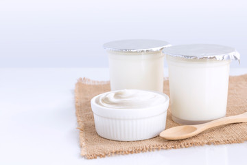 Healthy flavored yogurt in plastic cup and ceramic bowl with wooden spoon isolated on the white table with on gray background. With copy space for your text.