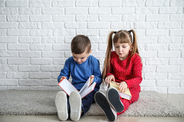 Cute little children reading books near white brick wall