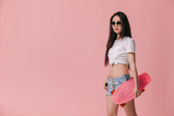 Fototapeta na wymiar beautiful sexy asian woman in sunglasses holding skateboard on pink background. copy space
