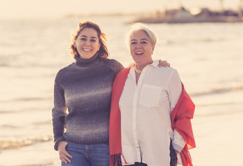 Portrait of beautiful older mom and mature daughter walking on the beach at autumn sunset