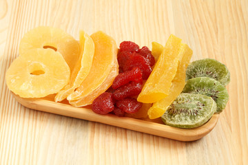 Dried pieces of kiwi, papaya, mango, pineapple and strawberry fruits, lying on a bamboo plate on a wooden table. Macro. Closeup