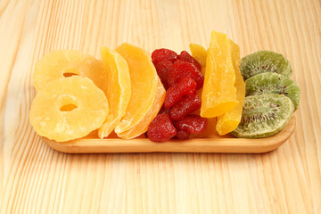 Dried pieces of kiwi, papaya, mango, pineapple and strawberry fruits, lying on a bamboo plate on a wooden table. Macro. Closeup