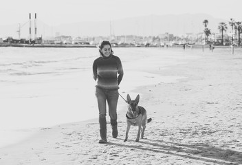 Happy attractive young woman with her german shepard dog walking on the beach at autumn sunset