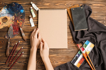 Hands of female artist, tools and paints on wooden background, top view