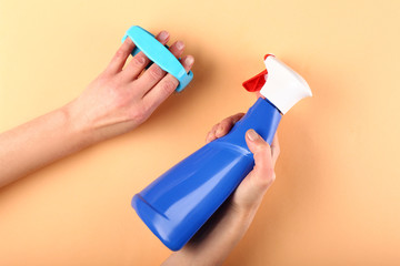 Hands of female janitor with brush and detergent on color background