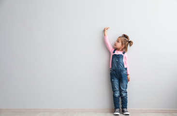 Portrait of cute little girl near light wall