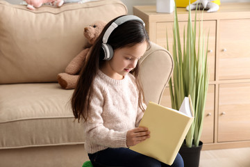 Cute girl with headphones reading book at home