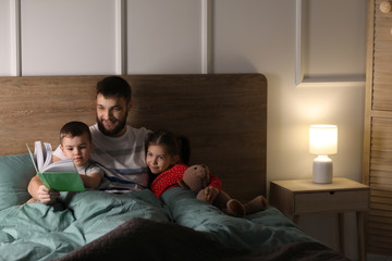 Young father reading book for his children in bed