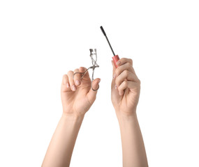 Female hands with manicure holding eyelash curler and mascara brush on white background