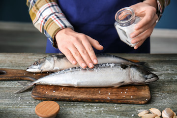 Woman preparing tasty mackerel fish on table in kitchen