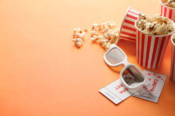 Obraz na płótnie Canvas Paper cups of tasty popcorn, tickets and cinema glasses on color background