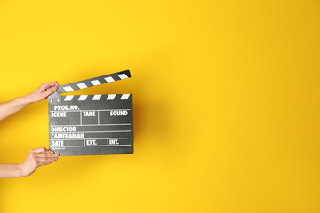 Female hands with cinema clapperboard on color background