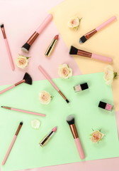 Obraz na płótnie Canvas Makeup cosmetic accessories products brushes, lipstick, pink flowers on pastel colors background. Flat lay. Top view. Copy space