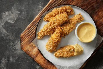 Wooden board with tasty nuggets and sauce on grey table