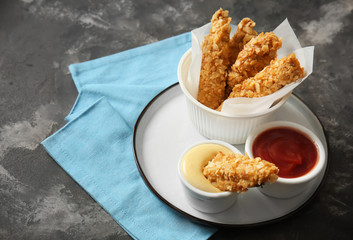 Plate with tasty nuggets and sauces on grey table