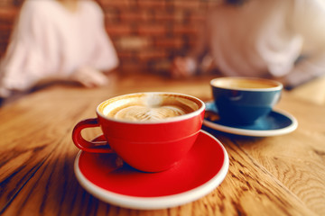 Close up of two cups of coffee on desk. In background blurred couple flirting.