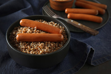 Bowl with tasty boiled buckwheat and sausages on table