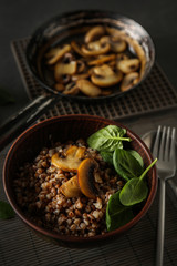 Bowl with tasty boiled buckwheat and fried mushrooms on table