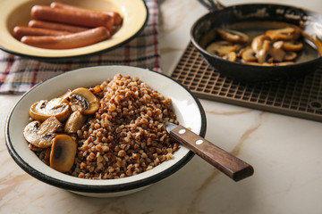 Bowl with tasty boiled buckwheat and fried mushrooms on table