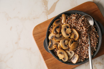 Pan with tasty boiled buckwheat and fried mushrooms on table