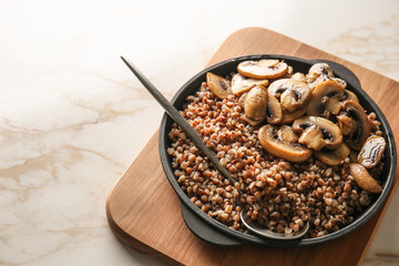 Pan with tasty boiled buckwheat and fried mushrooms on table