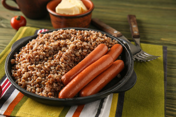 Frying pan with tasty boiled buckwheat and sausages on wooden table