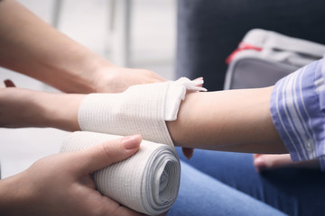 Woman applying bandage onto female arm, closeup