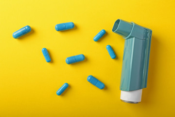Inhaler and pills on color background