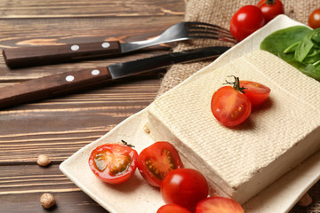 Plate with tasty tofu cheese and tomatoes on wooden table