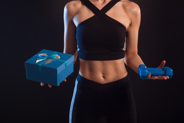 athletic girl holding dumbbells and gift box in her hands