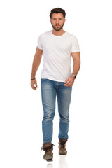 Serious Young Man In Jeans And White T-shirt Is Walking Towards Camera