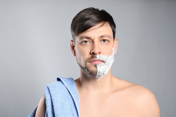 Handsome man with shaving foam on his face against grey background