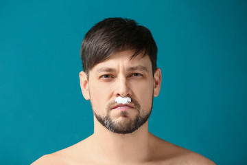 Bearded man with shaving foam on his face against color background