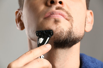 Handsome man shaving against grey background, closeup