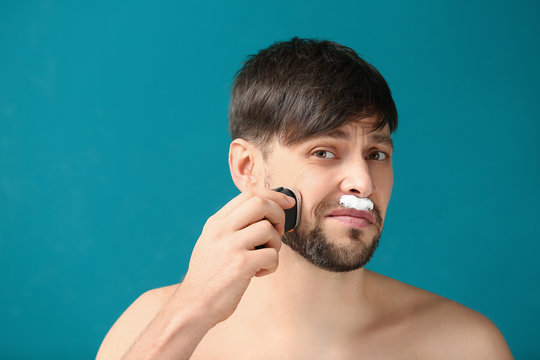 Regretful Man Using Electric Shaver Against Color Background