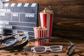 Movie clapper with film reel, popcorn and glasses on wooden table
