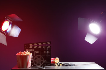 Movie clapper with film reel, popcorn and glasses on table
