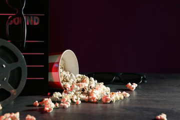 Overturned bucket with popcorn, movie clapper and glasses on grey table
