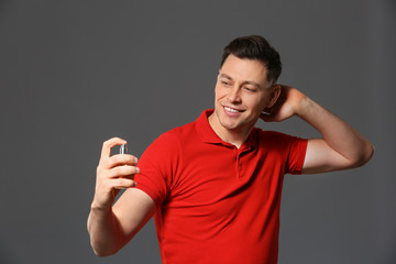 Handsome man with bottle of perfume on grey background