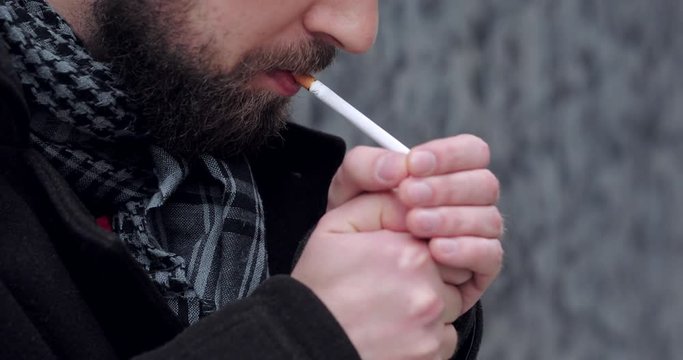 Bearded man walking on the city street and smoke cigarette 