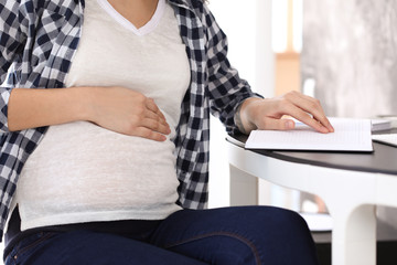 Beautiful pregnant woman with notebook sitting at table