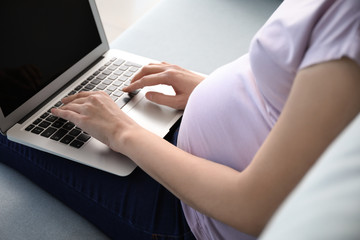 Beautiful pregnant woman using laptop at home, closeup