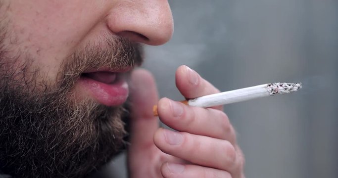 Bearded man walking on the city street and smoke cigarette 