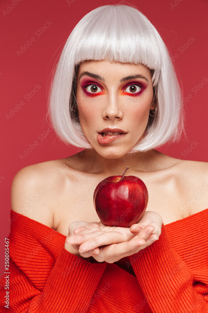 Poster Beautiful young woman isolated over red wall background holding apple.